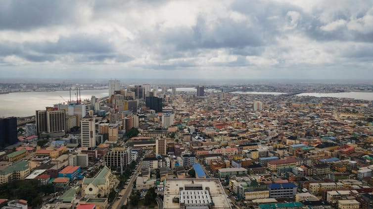 Aerial view of a vast urban development along water, skyscrapers mixing with more informal buildings, set against a cloudy grey sky. Aerial view of a vast urban development along water, skyscrapers mixing with more informal buildings, set against a cloudy grey sky.