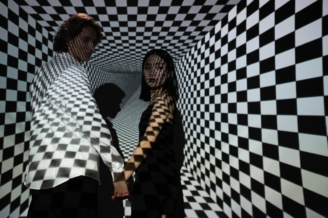 Free A man and woman stand in a checkered tunnel, creating a dramatic optical illusion. Stock Photo