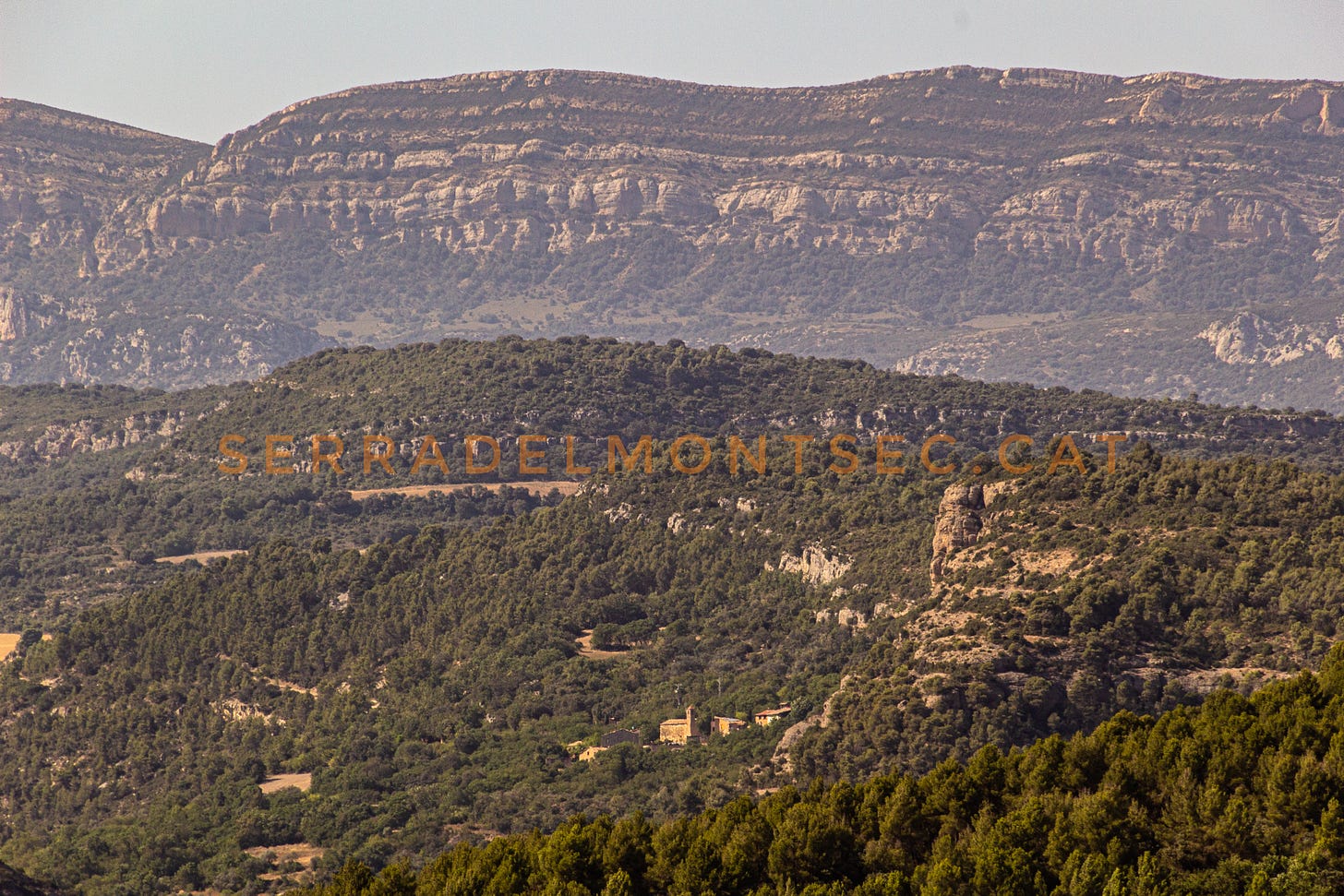 Els dos extrems de la Vall d’Ariet: a sota i al centre, el petit llogarret de Clua (o Clua de Meià) i, al mig a l’esquerra, les restes del castell de Castelló de Meia sobre el Serrat de les Artigues. Al fons el Montsec de Rúbies (o de Meià). La Noguera, Lleida, Catalunya.