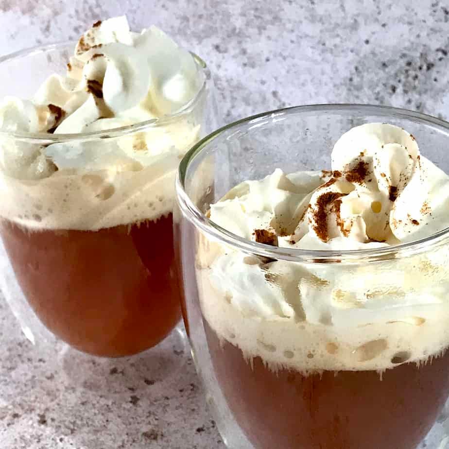 apple tea spiced topped with whipped cream in 2 glasses