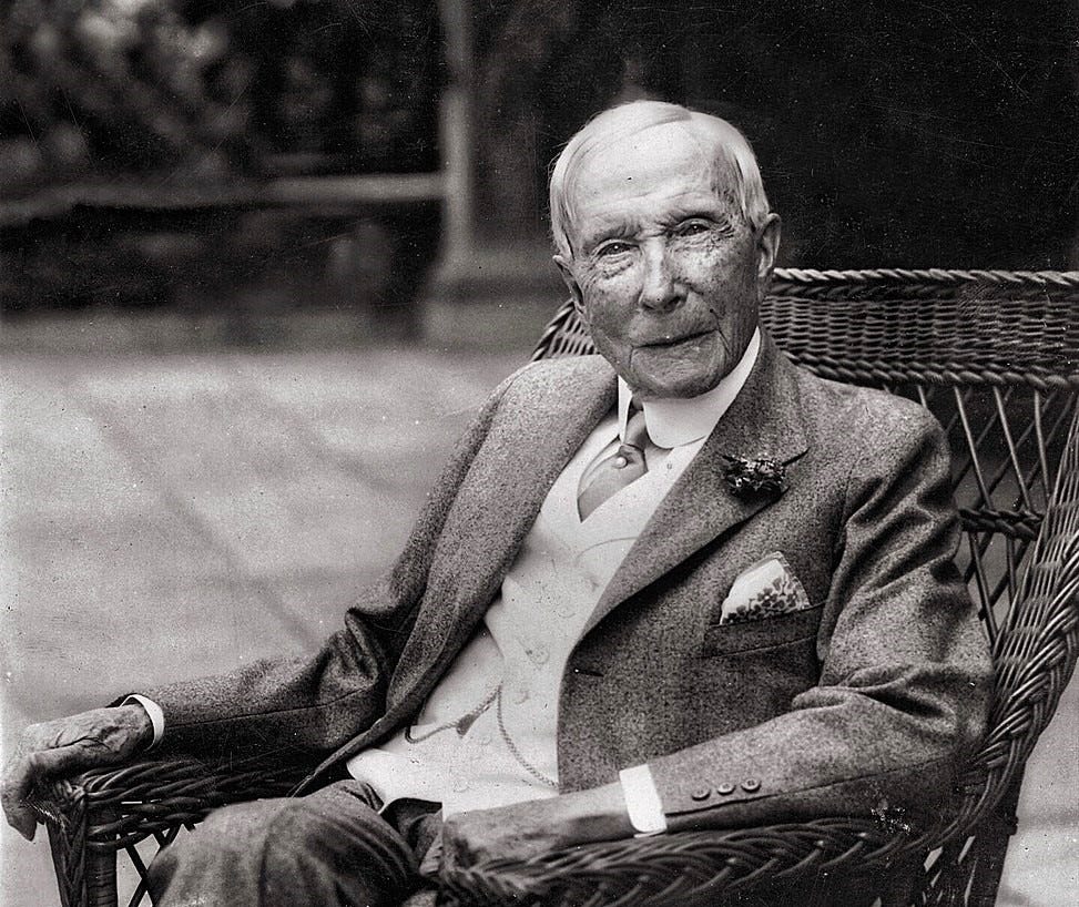 Black and white photo of an elderly John D Rockefeller sitting in a wicker chair