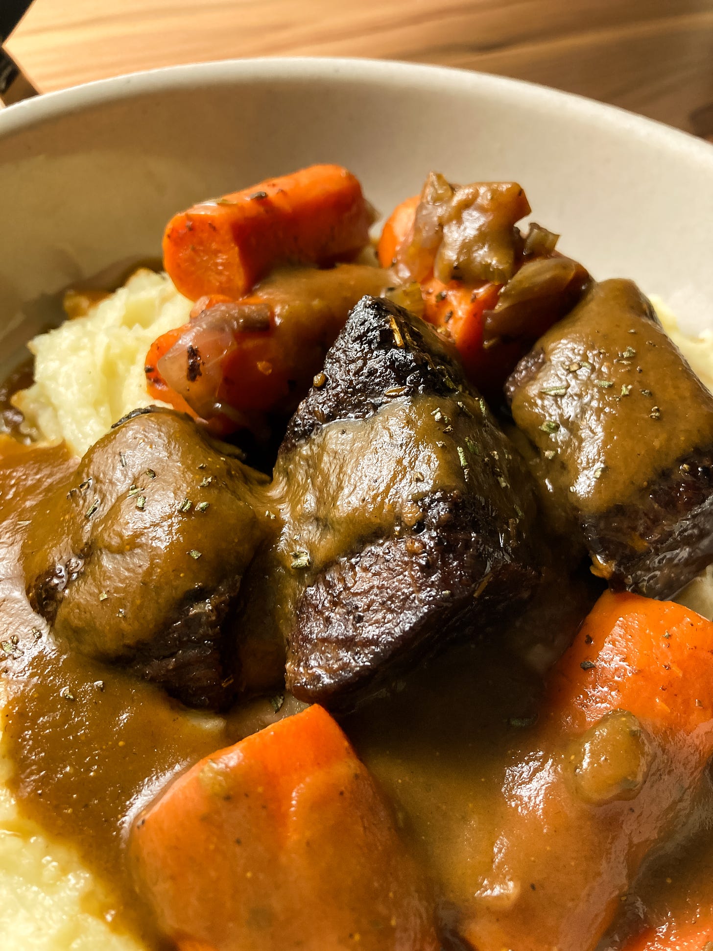 A super close shot of braised short ribs and carrots with gravy, all on a bed of mashed potatoes.