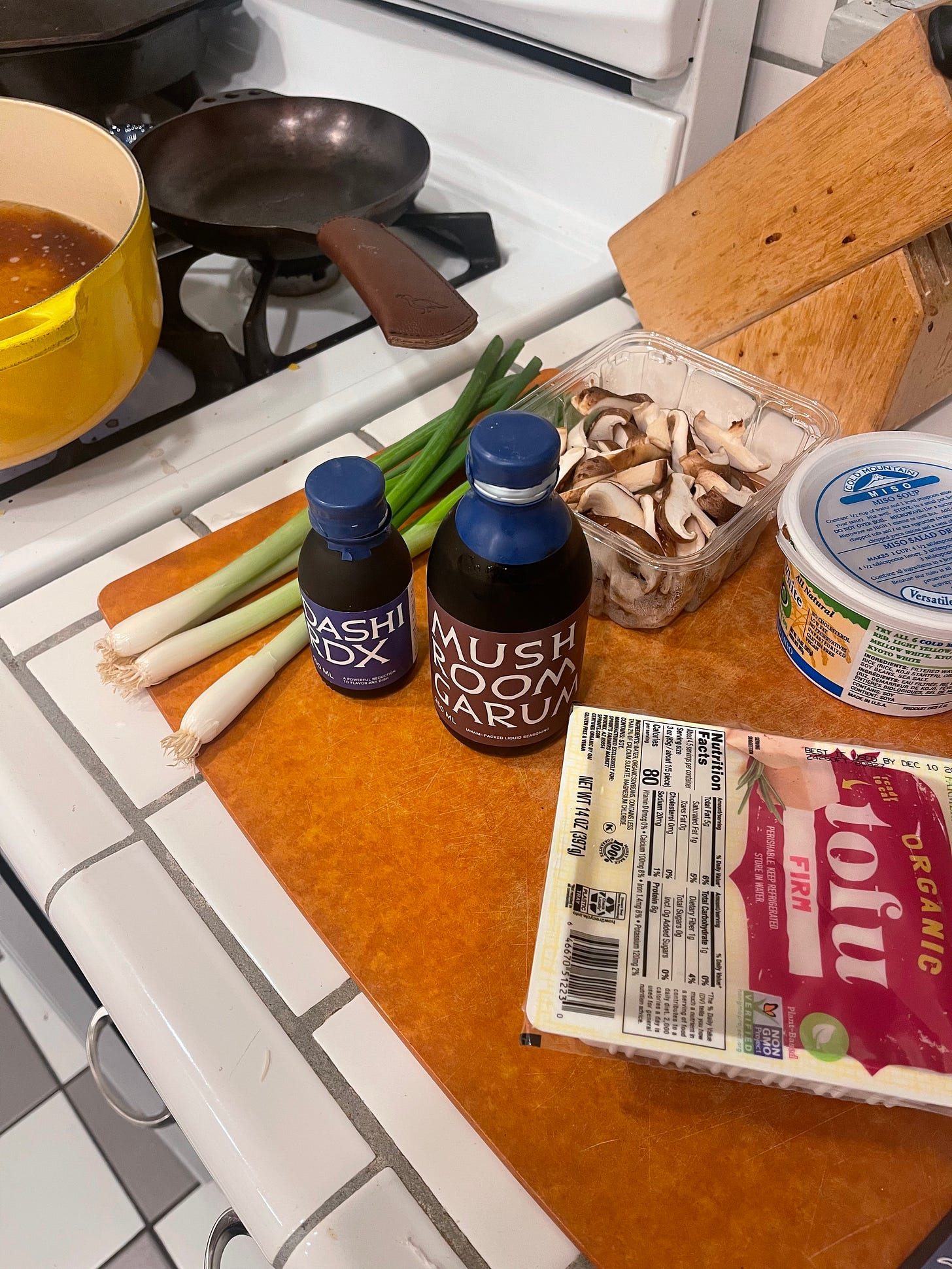 Kitchen cutting board with ingredients strewn about - tofu, scallions, miso, mushrooms and Noma Projects mushroom garam and dashi rdx