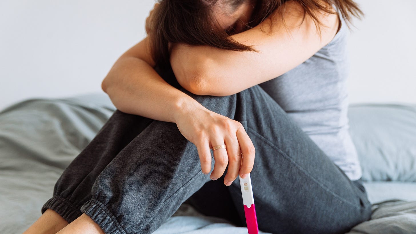 Woman sitting on a bed holding a negative pregnancy test. 