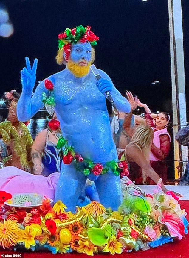 Naked man painted blue singing at the opening ceremony while sitting on a fruit plate