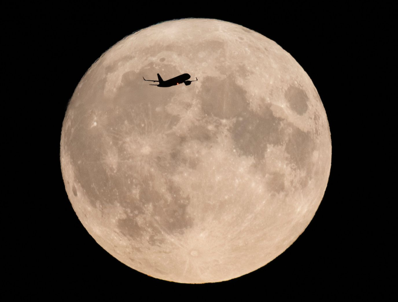 An aircraft passes in front of  a rare super blue moon, in London, England, on August 30.