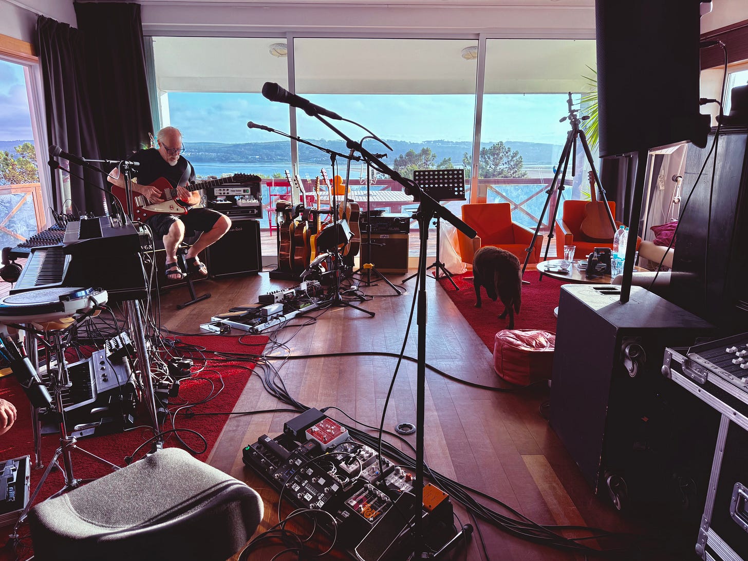 A man playing guitar in a music room full of equipment