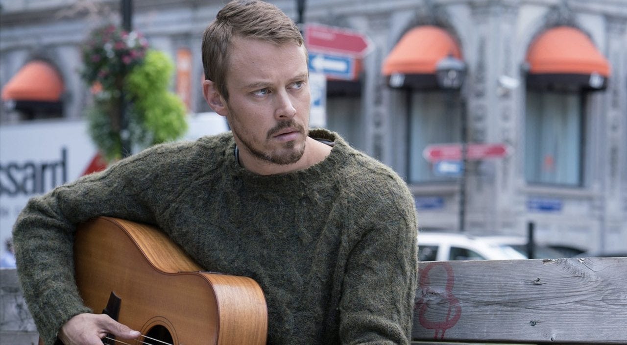 A man holds a guitar in the street in a scene from Patriot 