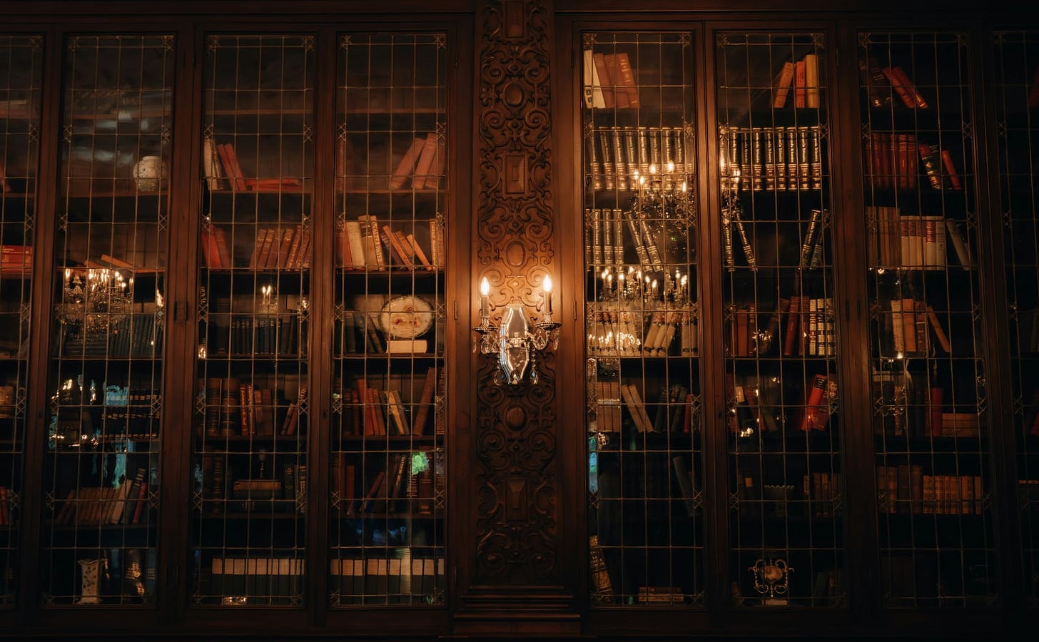 brown wooden bookshelve with glass fronts lit by a wall sconce