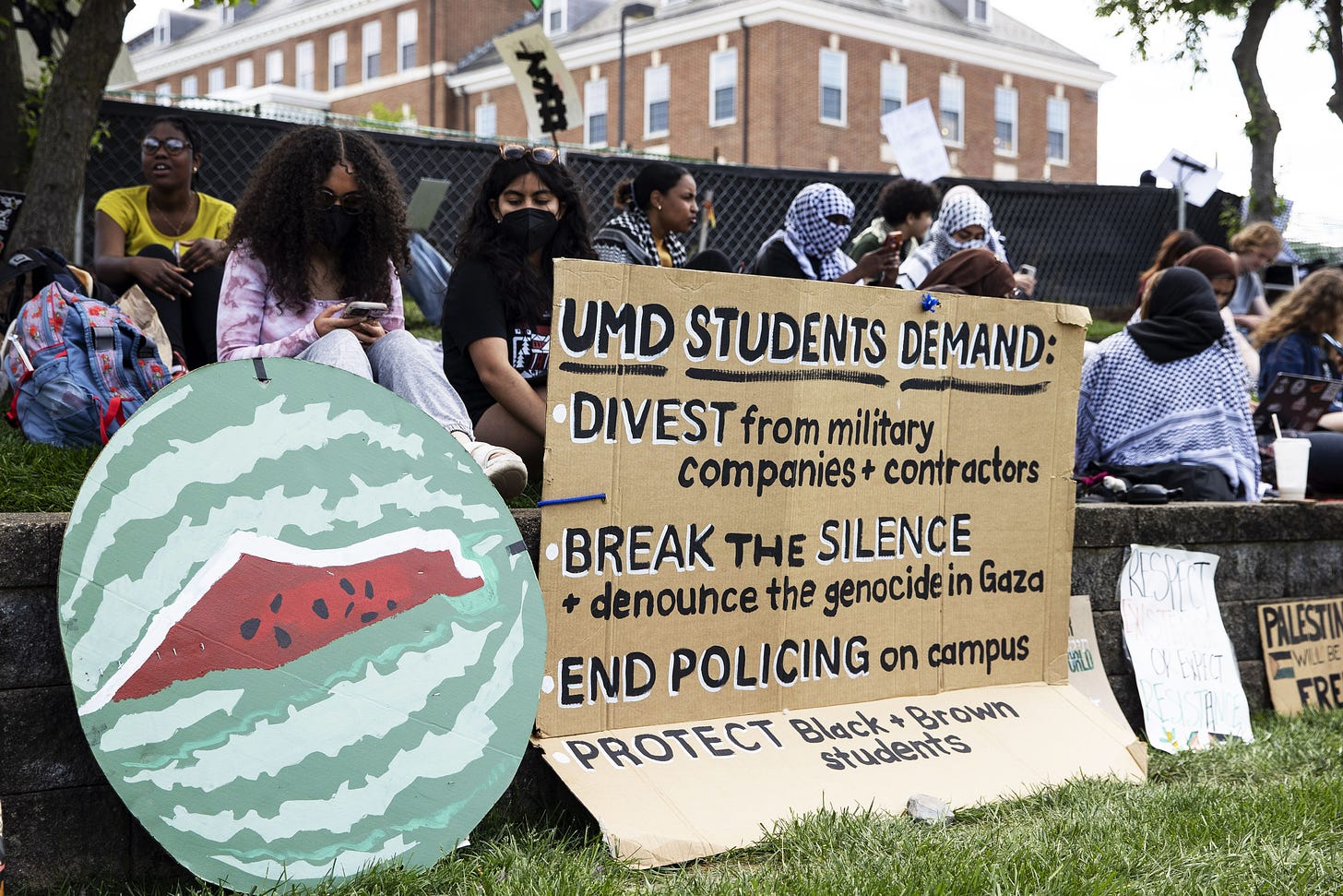 Students holding up a sign listing protestor demands on campus including divestment and ending policing on campus. 