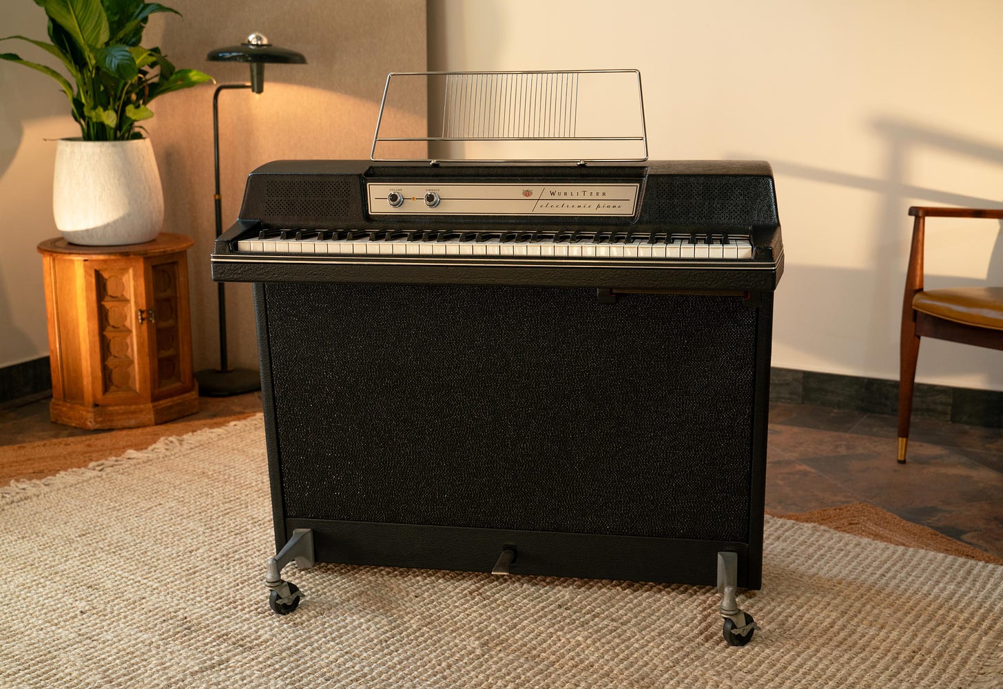 A black Wurlitzer 214 on a beige carpet, with a yellow chair, a large plant and a green light in the background.