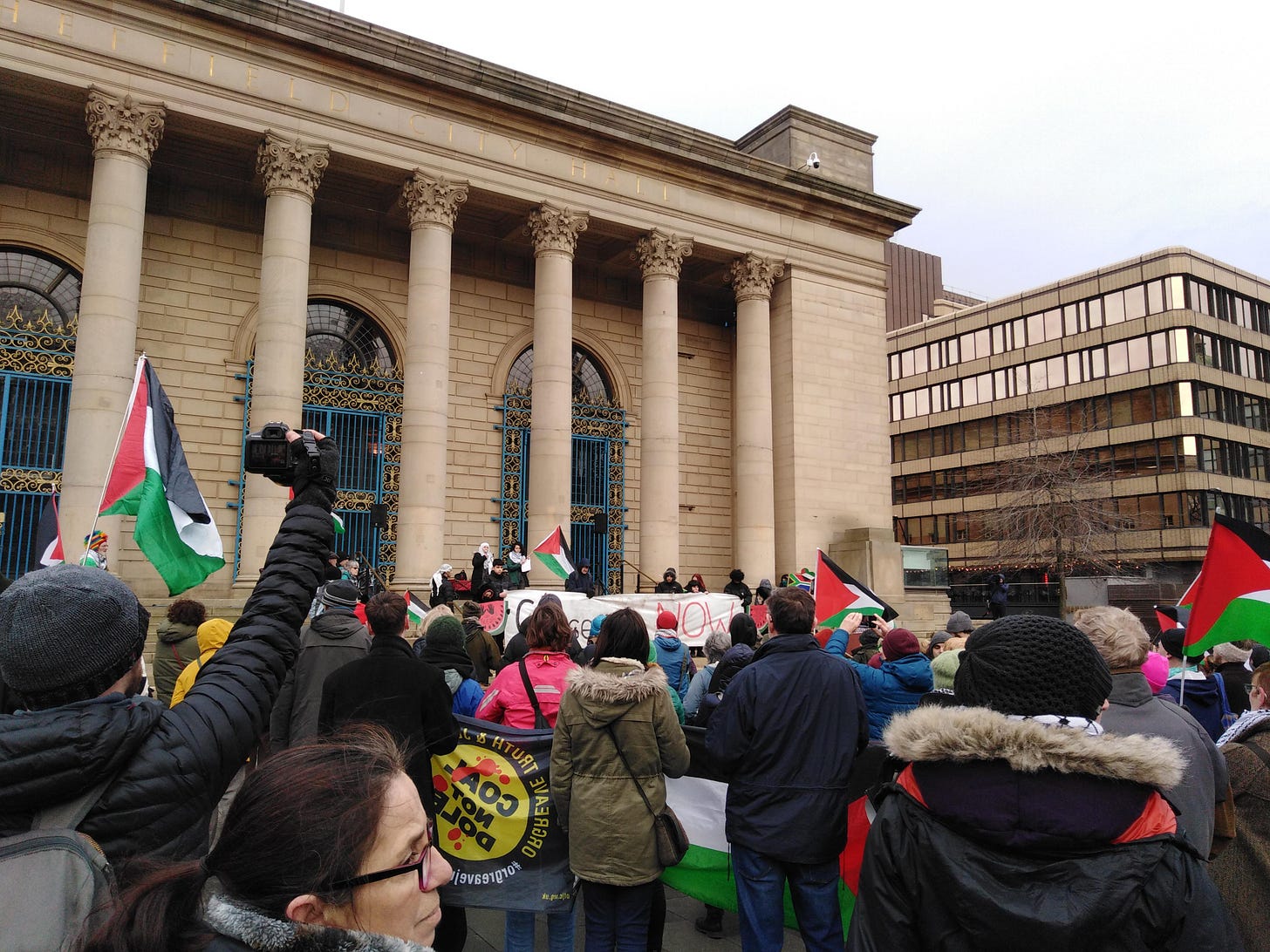 A rally outside Sheffield City Hall. Lots of people holding up red, black, white and green Palestinian flags.