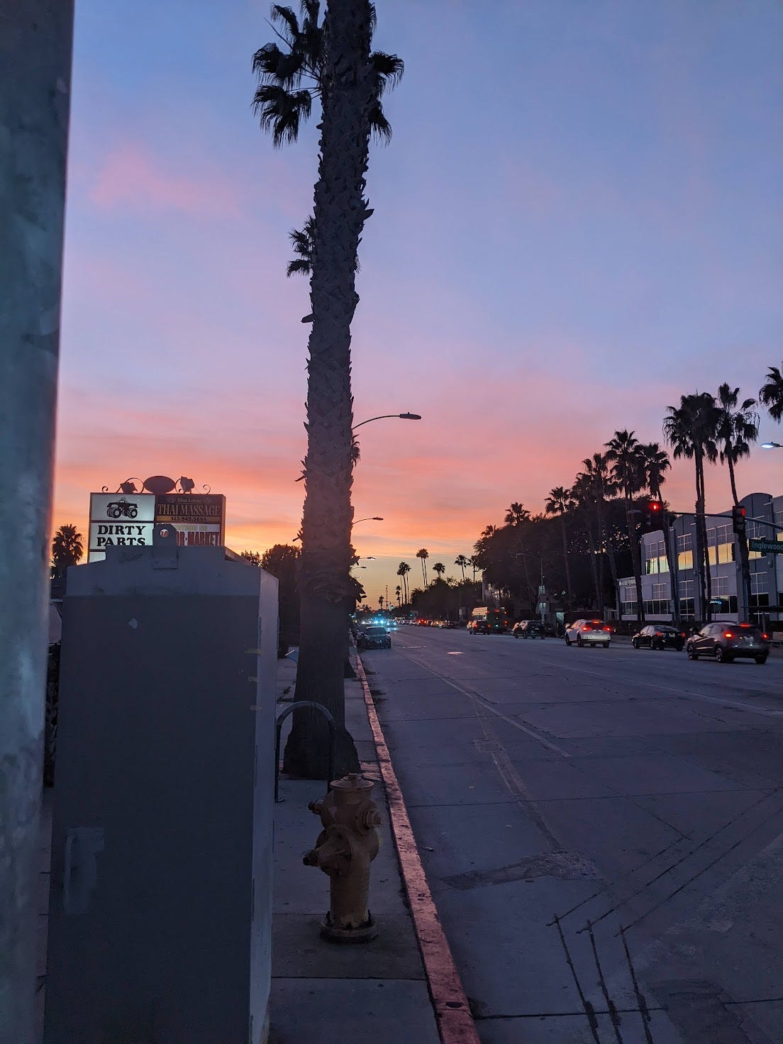 a boulevard in Los angeles with a bright orange to purple sunset sky in the background