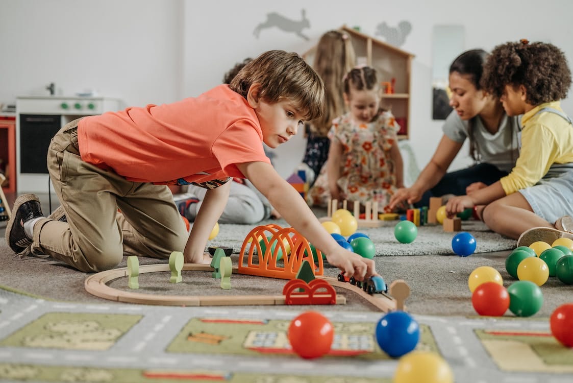 Free Boy in Orange Shirt Playing Train Toy on the Floor Stock Photo