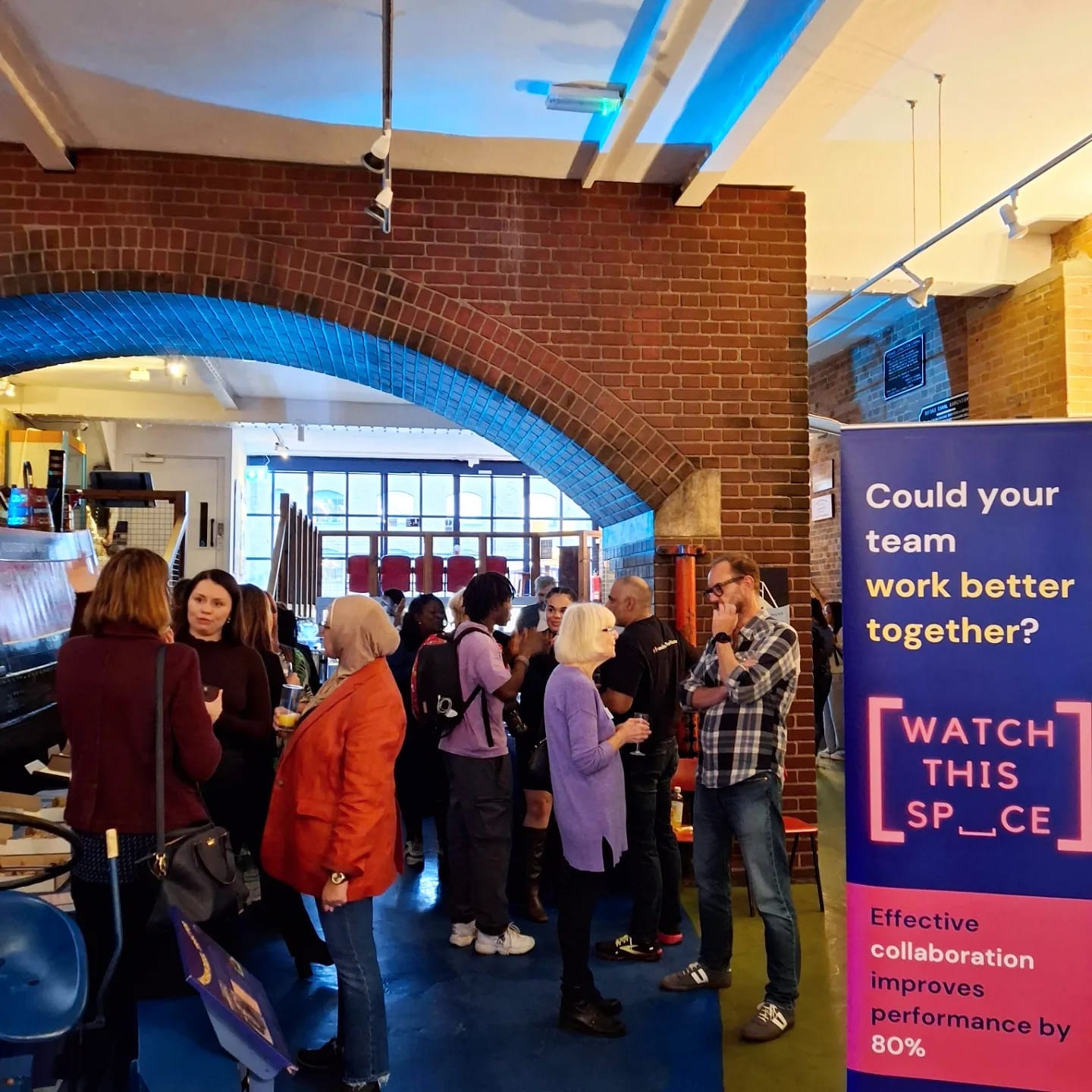 A room full of people talking next to a Watch This Space banner, with a canal boat to the side.