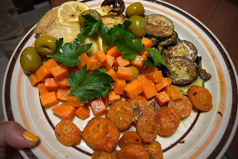 A plate of baked food, including carrots, zucchini, parsley, chicken, olives and sweet potato.