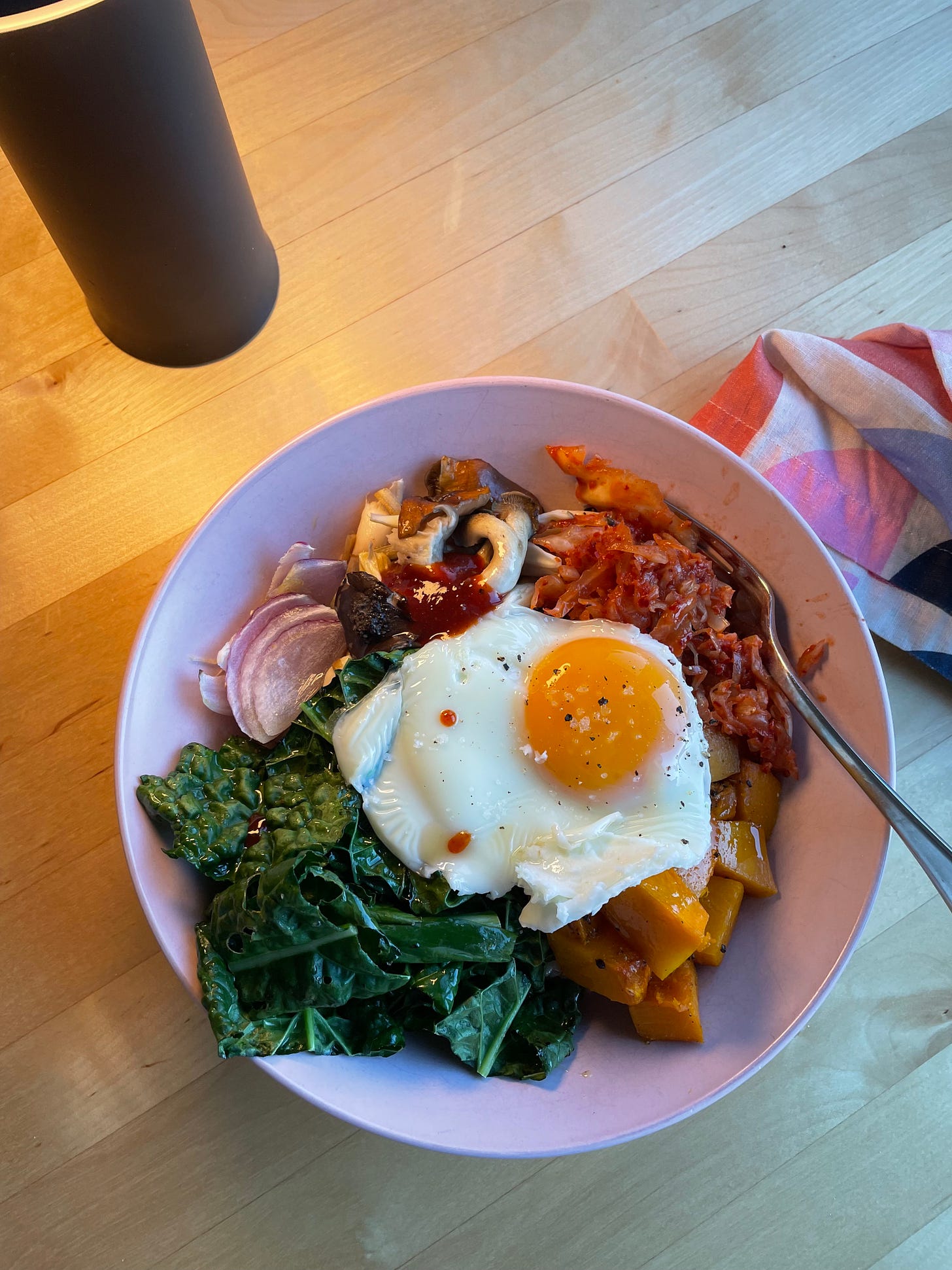 Pink bowl with roasted pumpkin, kale, red onion, served with a roasted egg and kimchi.