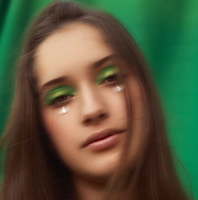 Very blurry photo of a woman wearing makeup on a green background.