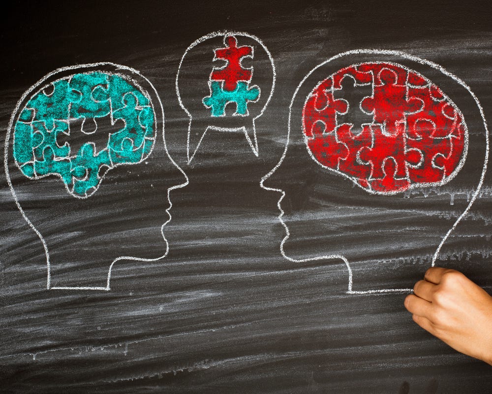 Blackboard and hand drawing heads in chalk looking at each other with different brains made of jigsaw puzzle pieces with one each coming together in a speech bubble