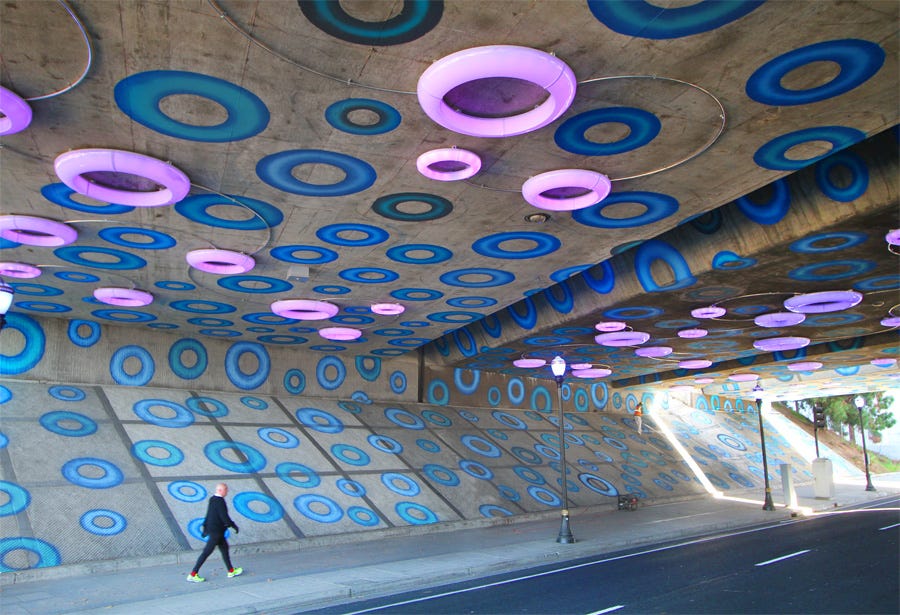 Sensing YOU is an interactive artwork utilizing light and paint to define a major downtown gateway in San Jose CA. The installation is defined by over 1000 painted circles and 81 individually controlled illuminated rings that play a variety of patterns and low-resolution mapped video over the ceiling surface of the I-87 highway underpass. The patterns are activated by pedestrians and bicyclists moving through the space- setting off pre-programmed sequences.