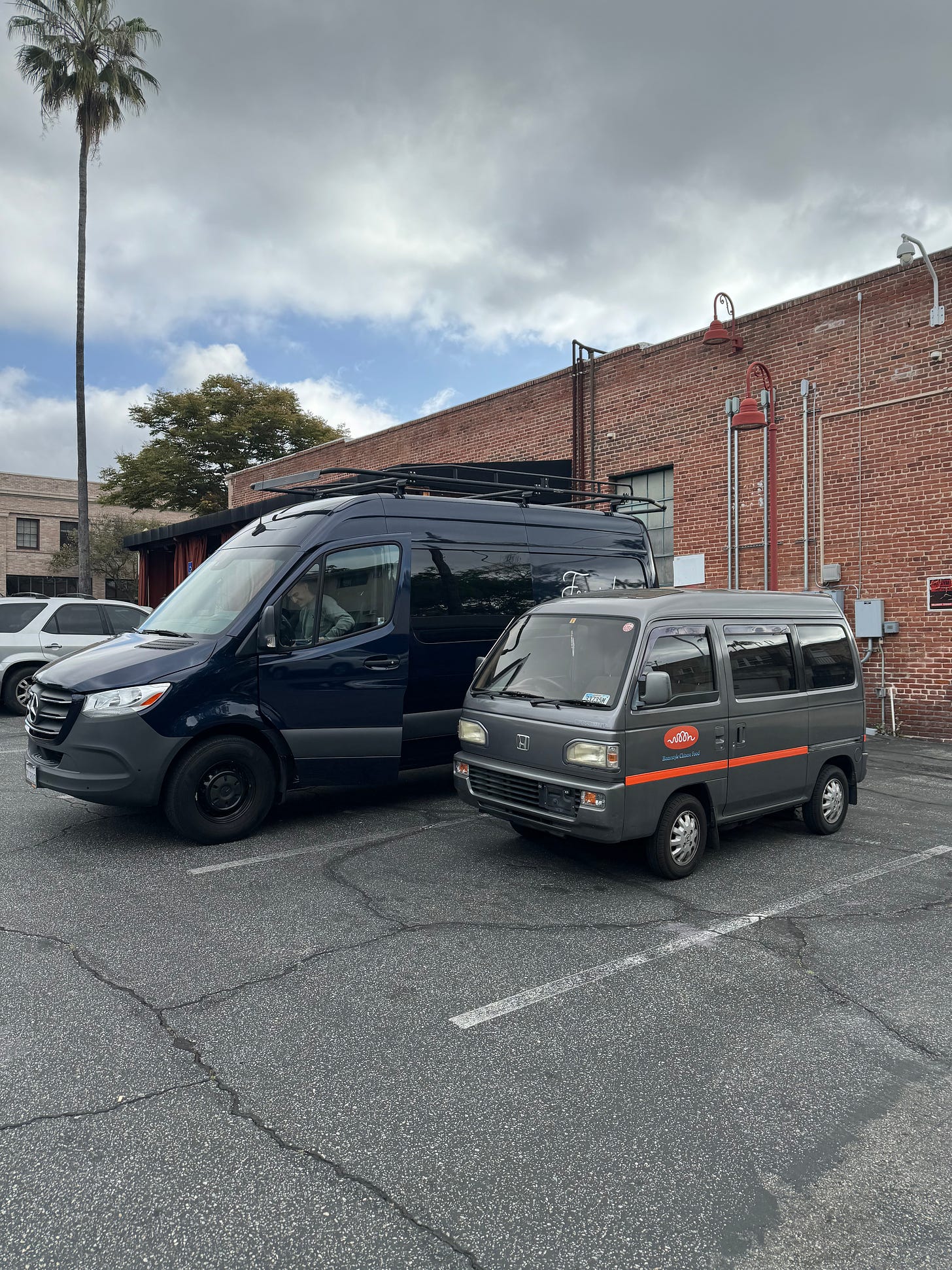 A 1991 Honda Acty Street parked next to a Mercedes Benz Sprinter van