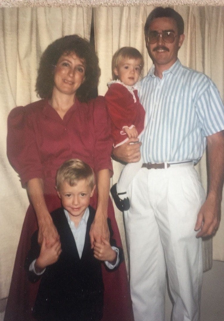 Family of four. Dad on the right holding baby, who is Sawyer. Mom standing on the left. Sawyers brother standing between them. He is young. 