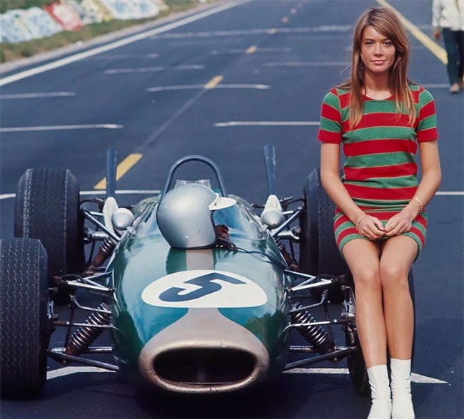 Movie still from Grand Prix. Francoise Hardy poses on a race car on a track.