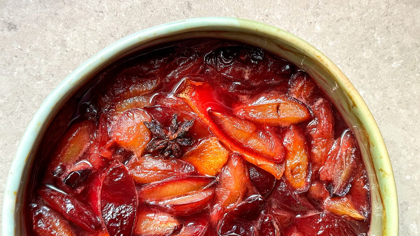 A bowl of roasted plums with orange and star anise.