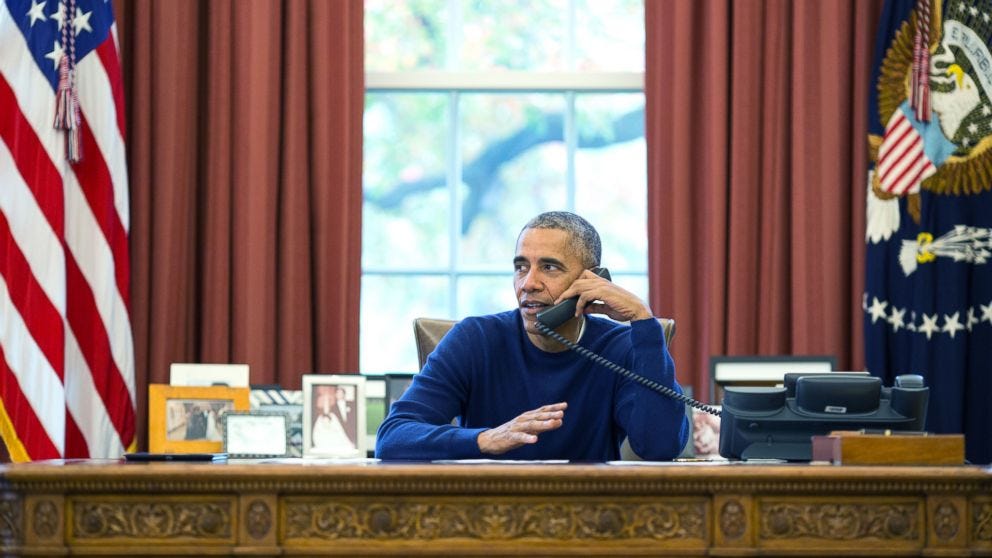 This image shows a 24 November 2016 photo of President Barack Obama, dressed in a blue sweatshirt, sitting at the Oval Office's Resolute Desk while talking on the phone with American soldiers stationed around the world. This image shows a 24 November 2016 photo of President Barack Obama, dressed in a blue sweatshirt, sitting at the Oval Office's Resolute Desk while talking on the phone with American soldiers stationed around the world.