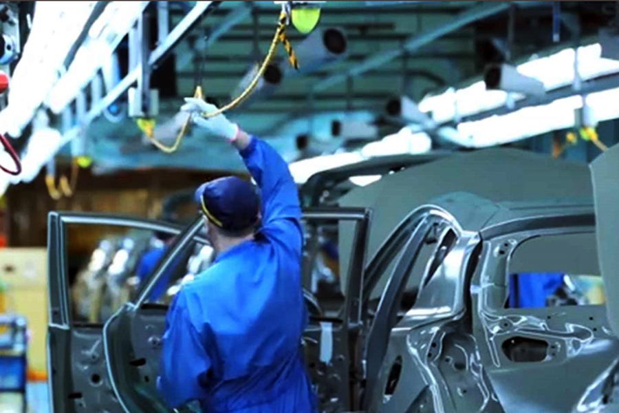 A photograph of a person in a car manufacturing plan pulling on a yellow cord above their head