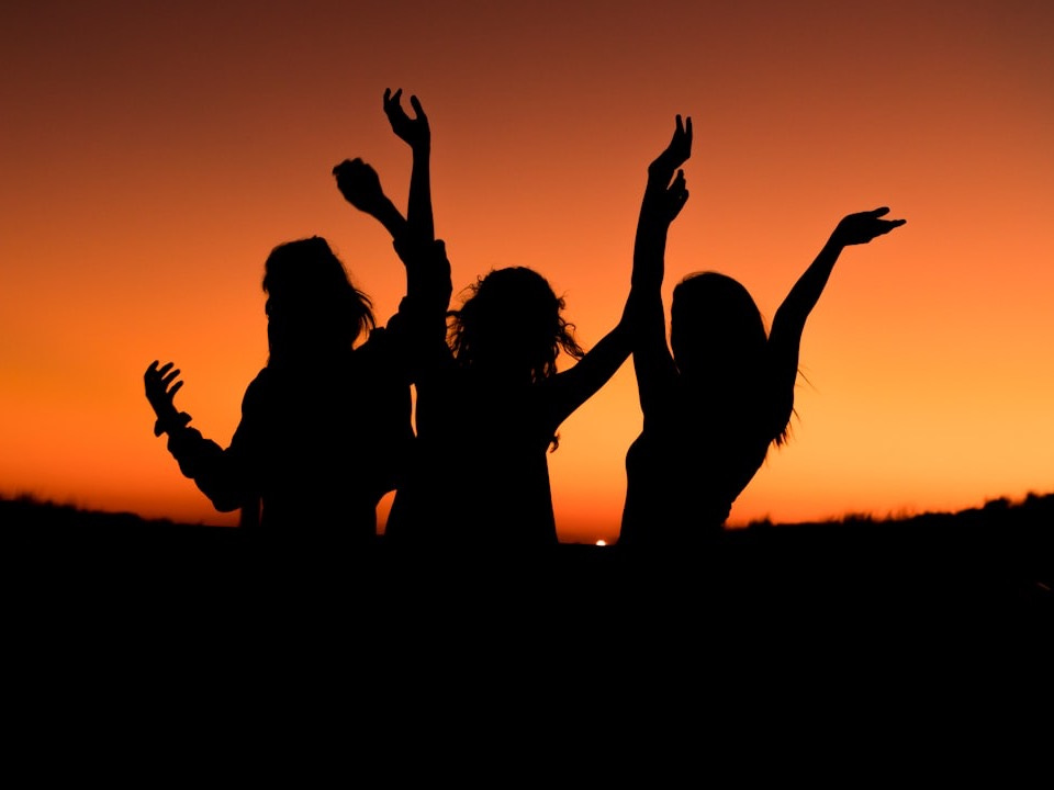 silhouette of three woman with hands on the air while dancing during sunset