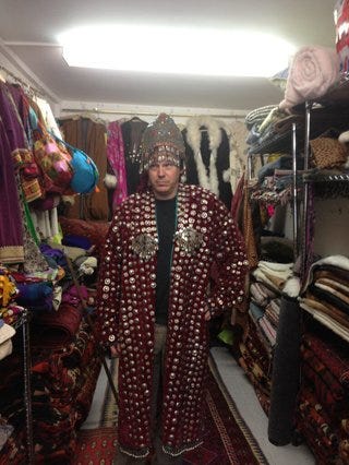 David Graeber dressed in red gown covered in sewn on coins and wearing a tasselled metalic headdress