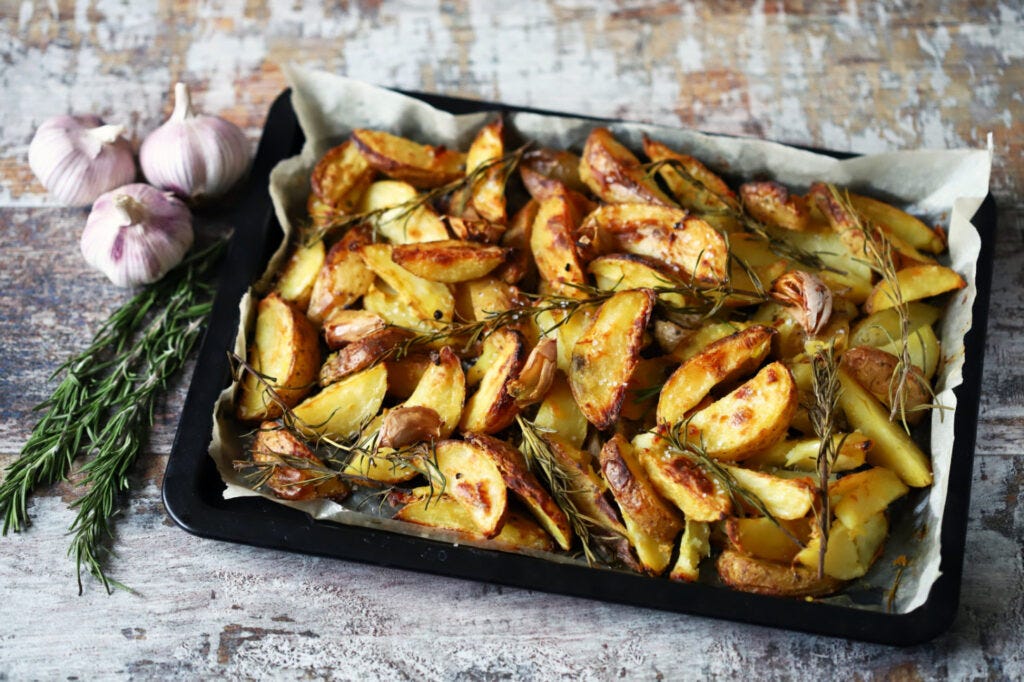 1456x970 px image for Easy Roasted Potatoes with Garlic and Rosemary showing a pan of roasted potatoes with garlic bub and srosmary sprig at the side.