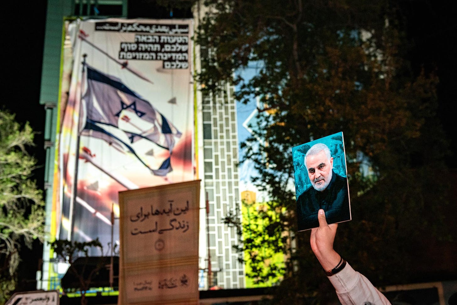 An Iranian pro-government supporter holds up a picture of slain Gen. Qassem Soleimani at Palestine Square in Tehran, on April 14, 2024 in front of an anti-Israel sign