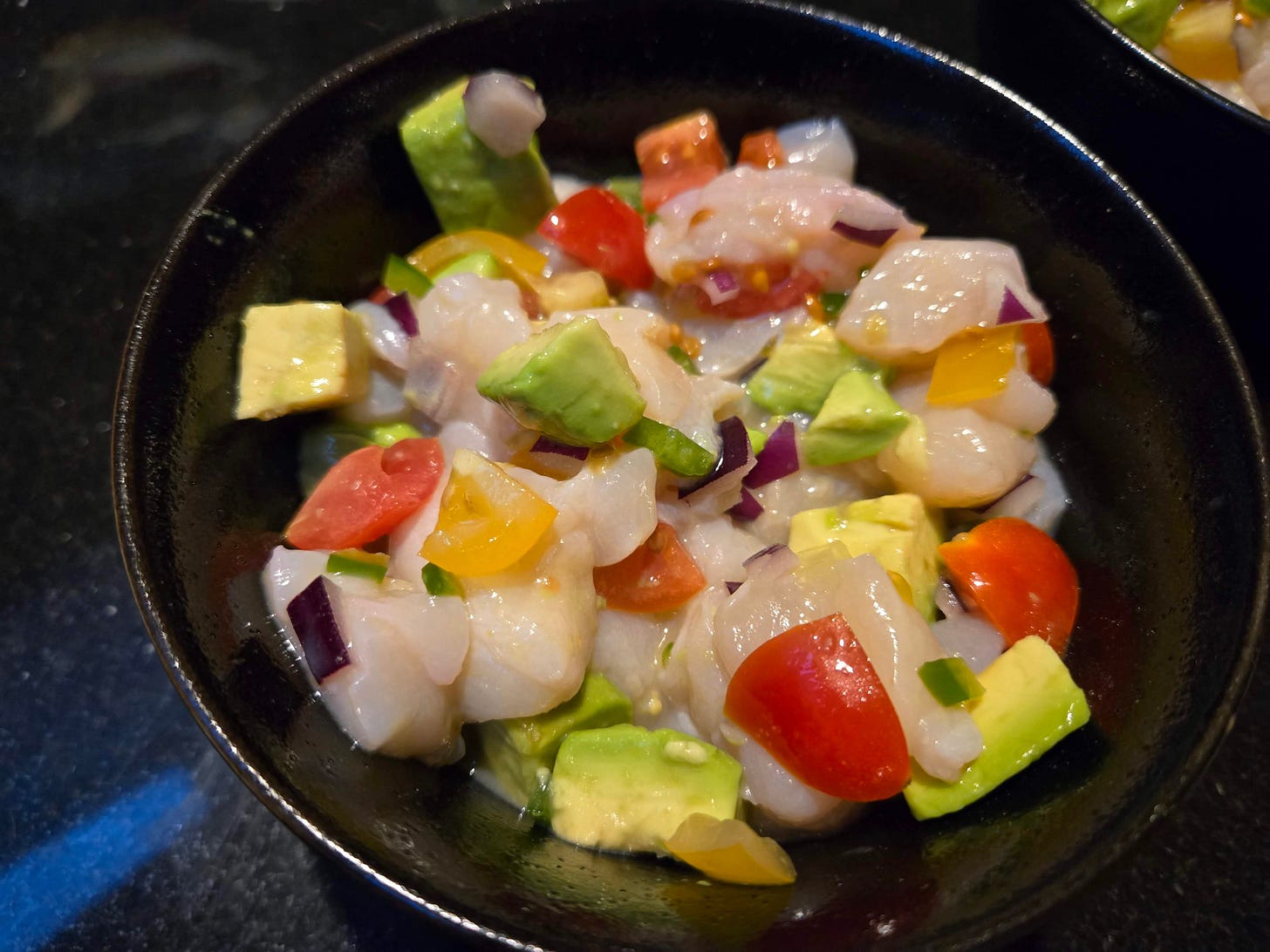 Scallop ceviche in a black bowl.