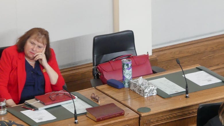 A red bag sits on an empty desk in the back row of the House of Assembly