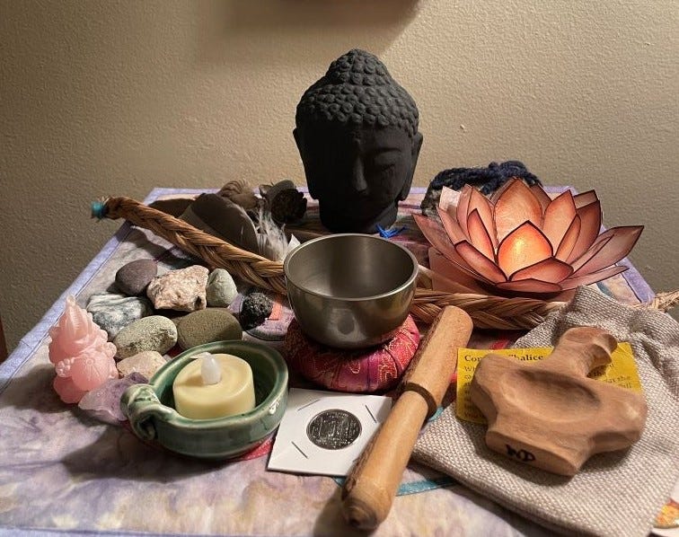 A carved wooden chalice, singing bowl, braided sweetgrass, and Buddha head sculpture, along with stones, feathers, and other items.