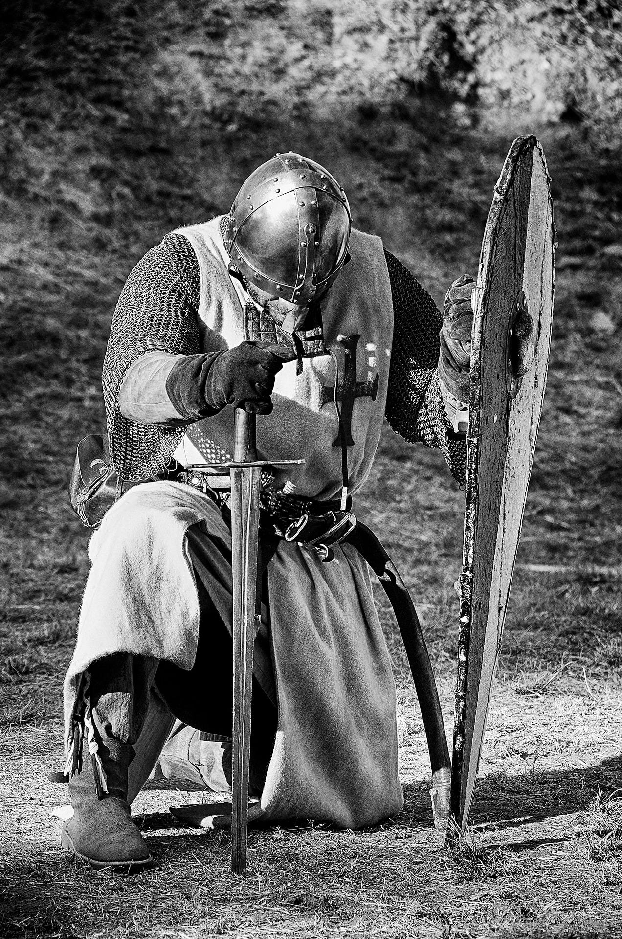 A medieval knight, with sword drawn, at prayer in a forest.