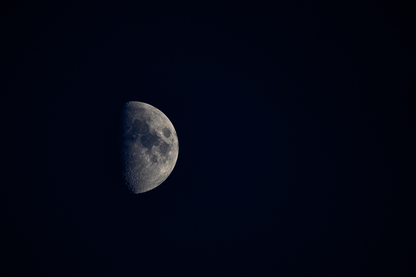 An image of the moon in a dark blue almost black sky with half of the moon not visible (the darker side of the moon).