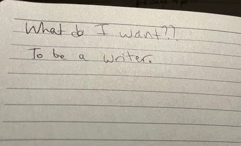 A white lined notebook page with the words "What do I want? To be a writer" written in black ink.