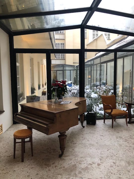 Photograph of a grand piano in a conservatory with patio furniture covered in snow in background