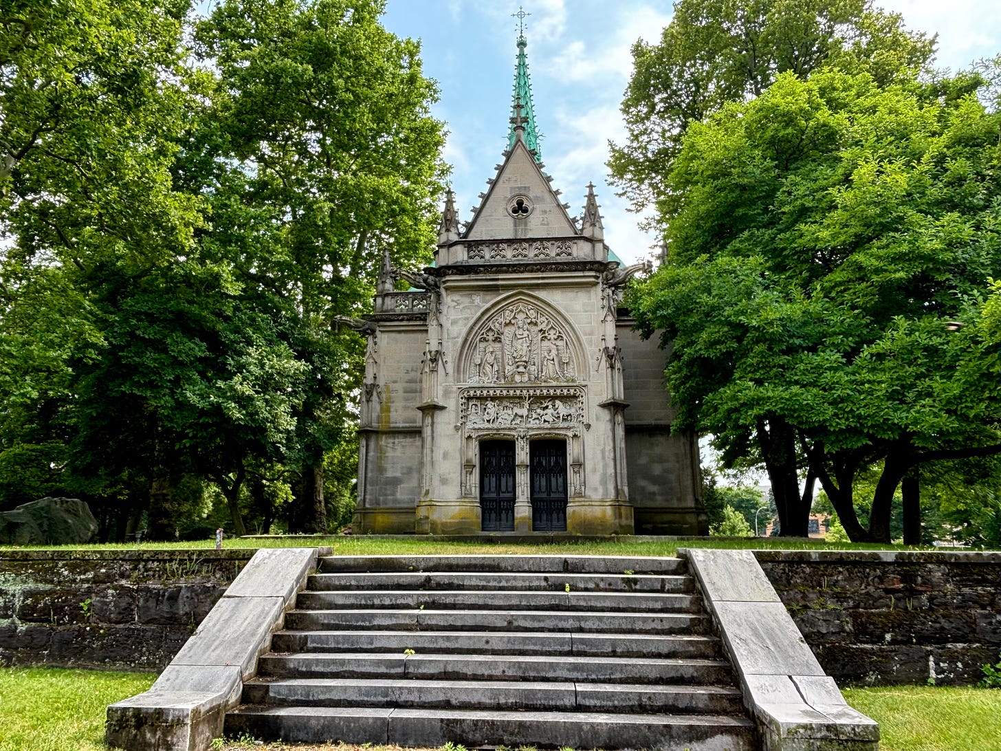 An ornate-style chapel with multiple relief sculptures set among green trees.