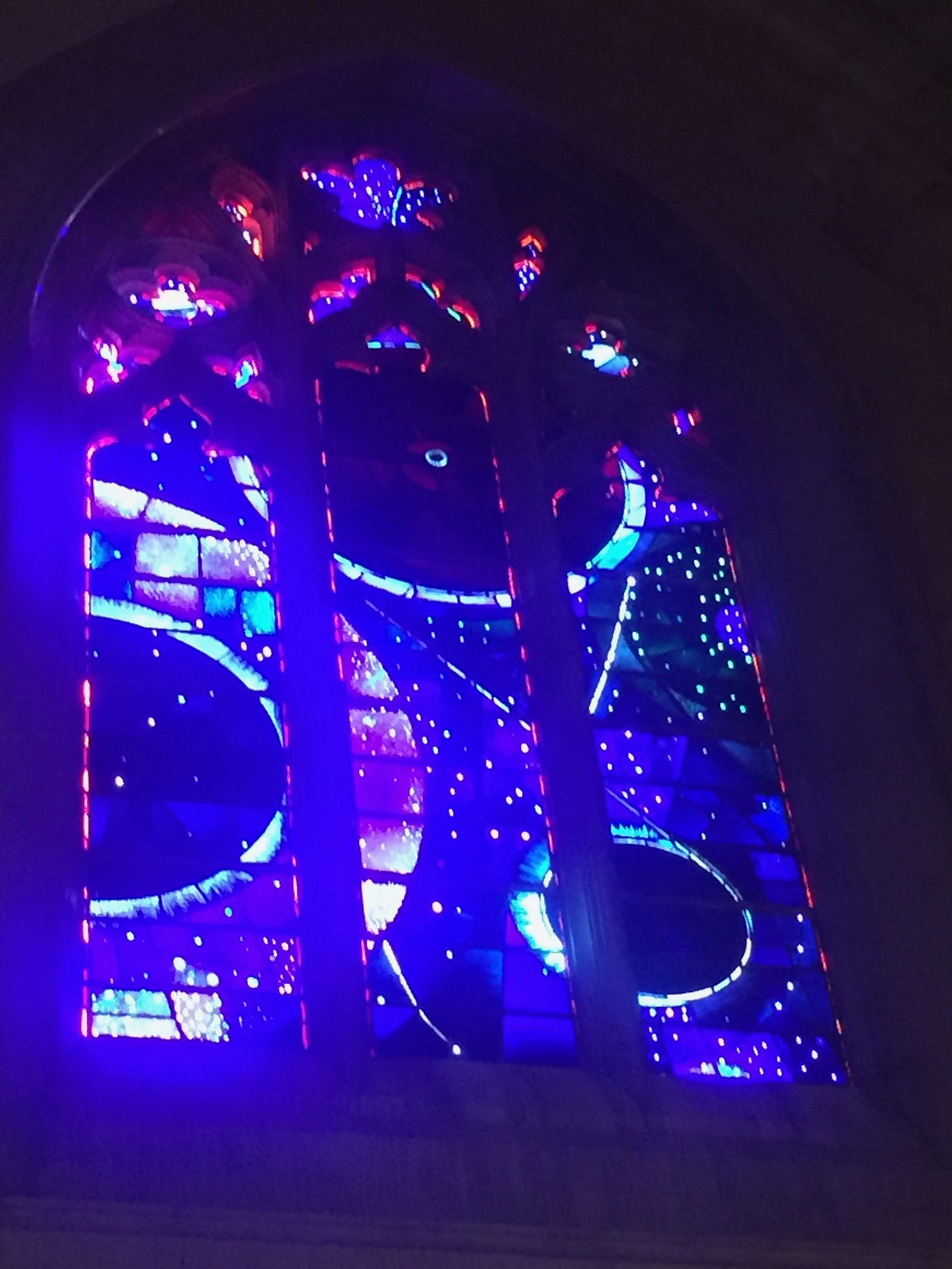 The space window at the National Cathedral, a beautiful stained glass window in dark purples and reds. A tiny stone is in the upper center.