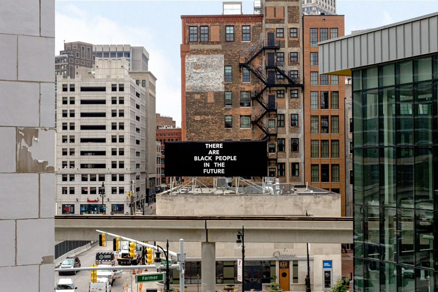 Colour photo of a solid black rectangular text artwork by Alisha B. Wormsley on the roof of a downtown building in the USA with tall buildings in the background. The billboard has white text in large capitals “THERE ARE BLACK PEOPLE IN THE FUTURE”. 