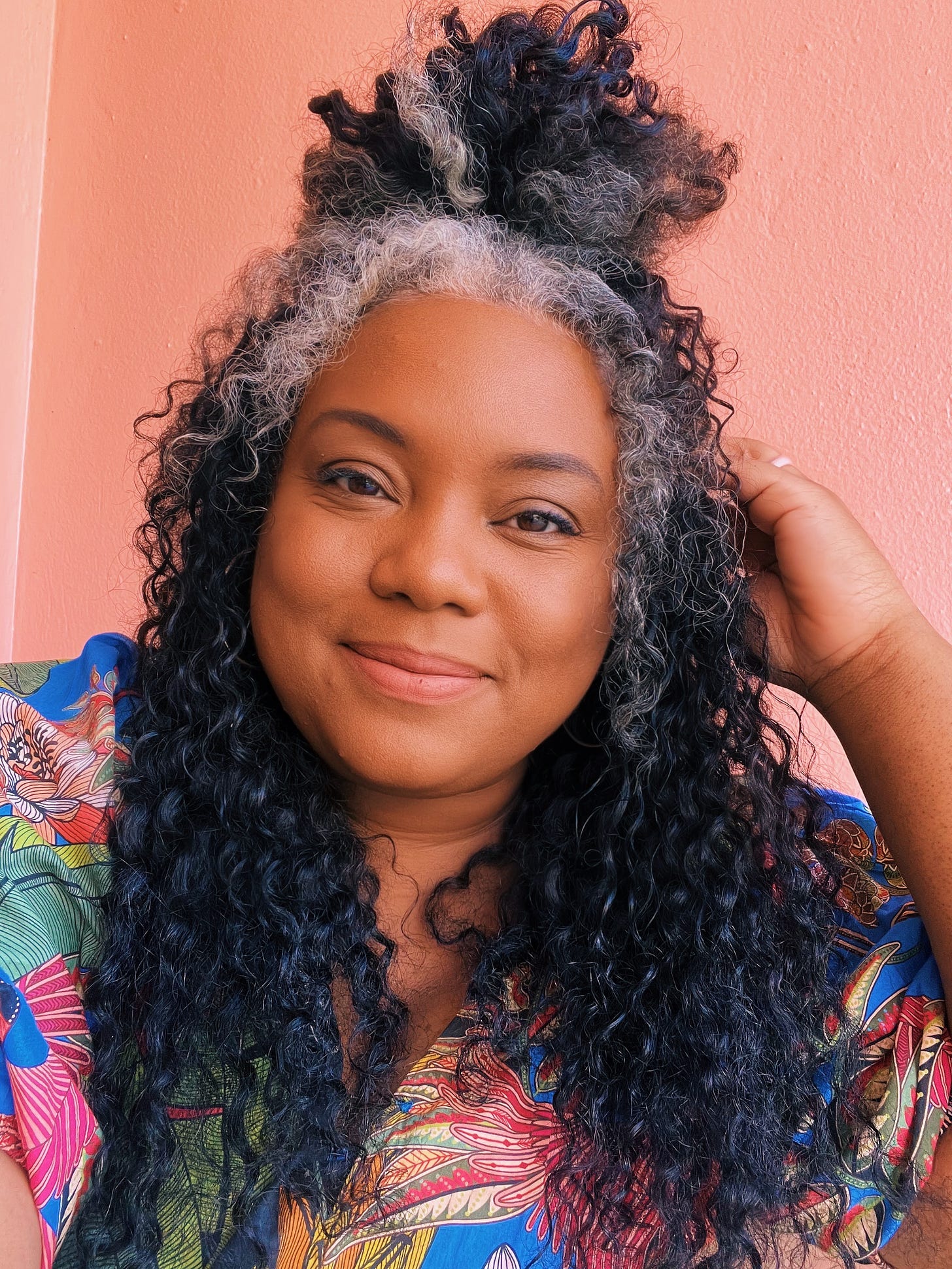 Morgan Harper Nichols smiles at camera. She is a black woman with curly black and gray hair wearing a colorful floral top.