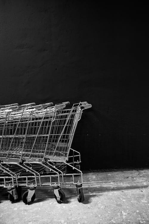 Free Black and white white of empty shopping trolleys standing on asphalt near black wall of supermarket Stock Photo