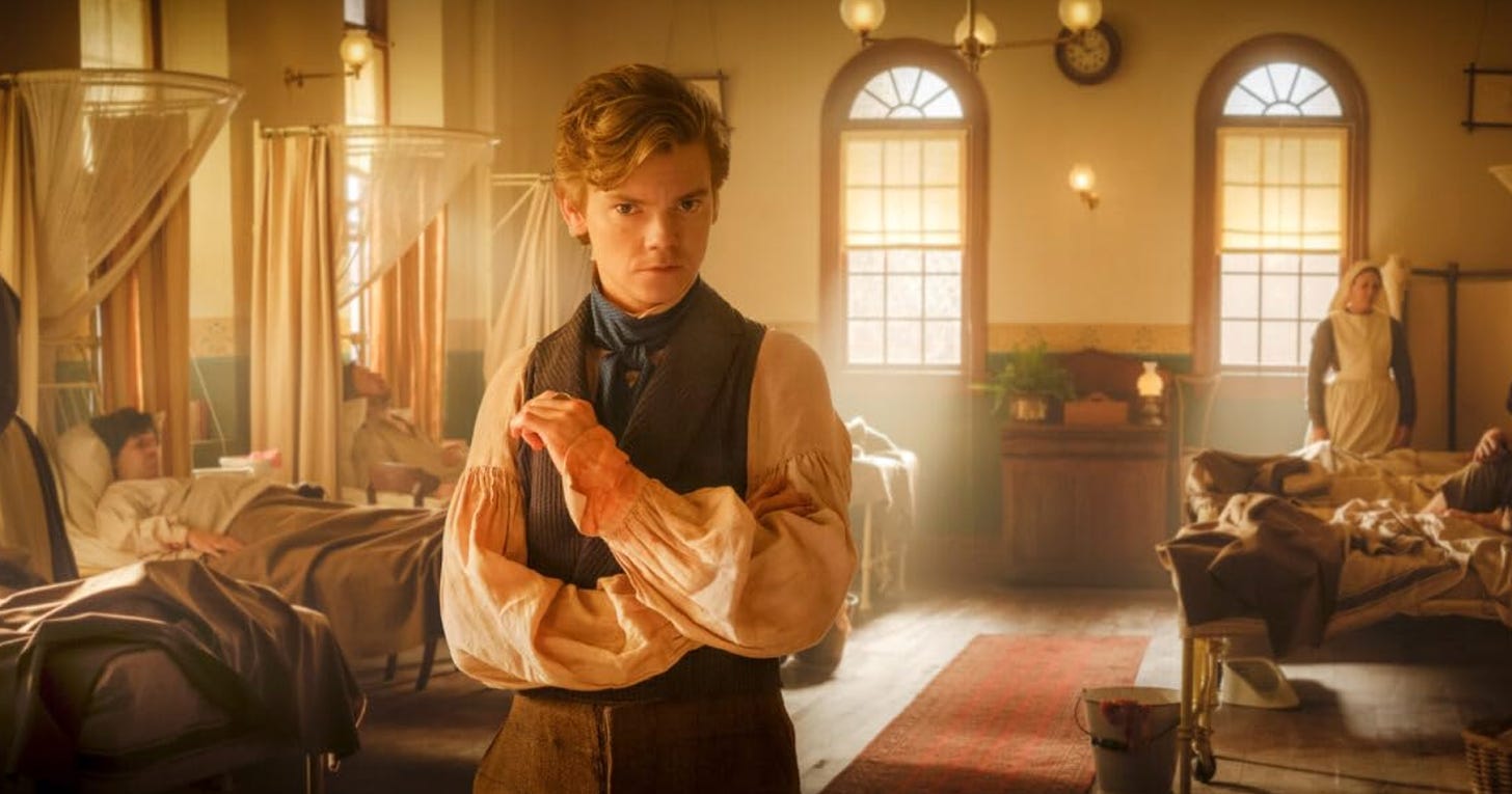 Thomas Brodie-Sangster in The Artful Dodger. He stands facing the camera with an enigmatic look in a medical ward