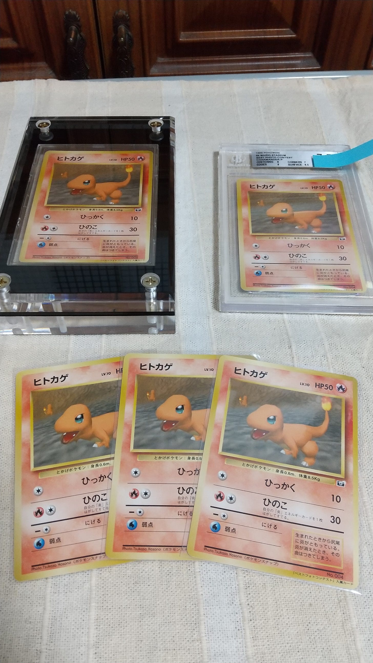 Five copies of Tsukasa's Charmander card. One copy inside of an acrylic frame, one graded copy, and three sleeved cards