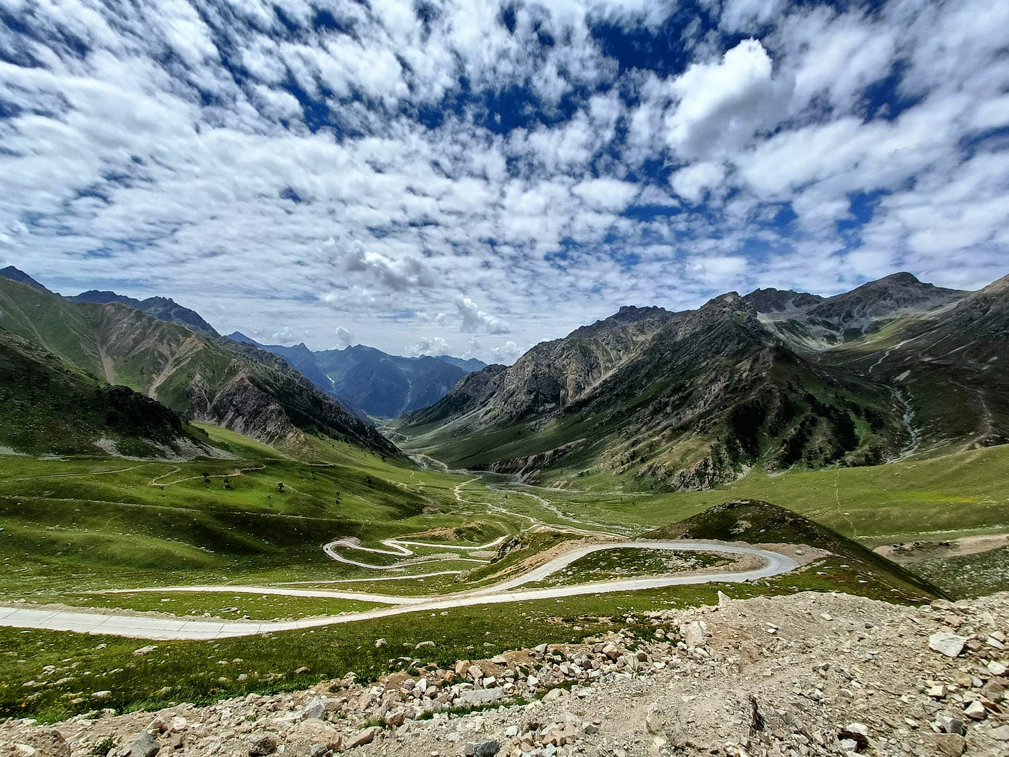 winding path amid green valleys with mountains and white clouds winding path amid green valleys with mountains and white clouds