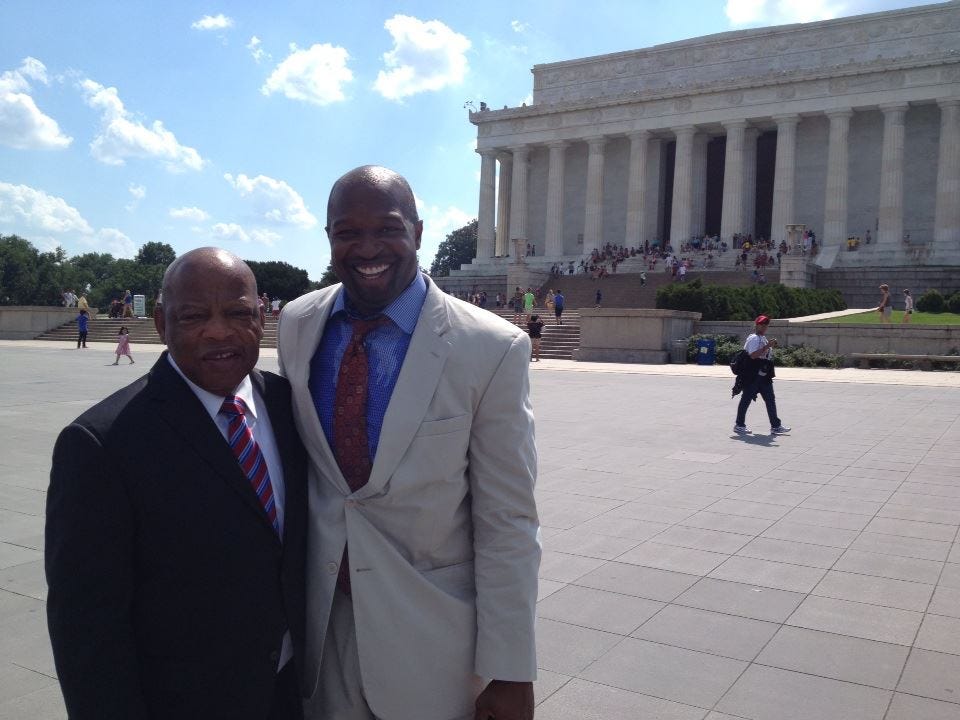 two men standing in front of the Lincoln Memorial on a sunny afternoon. One man is Rep. John Lewis